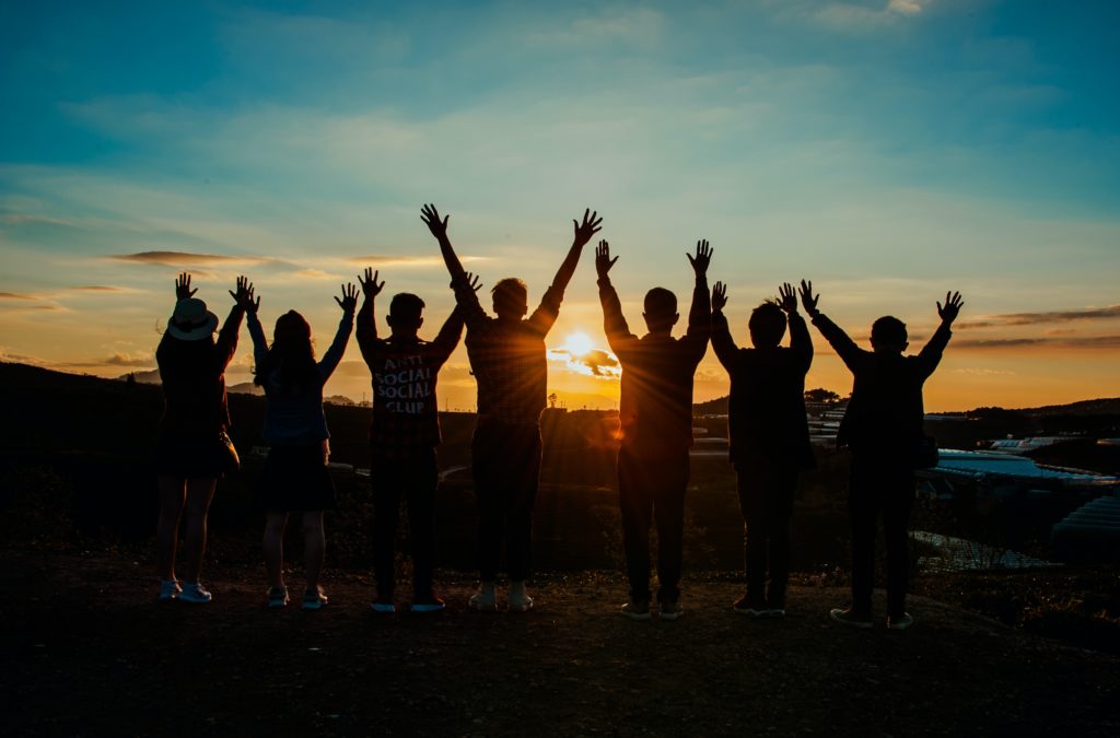 group with hands up at sunset