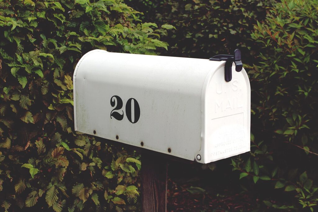 A white mailbox with the number 20 on it sits among deep green foliage