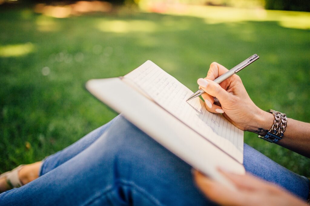 a person sits outside on a sunny day writing in a notebook