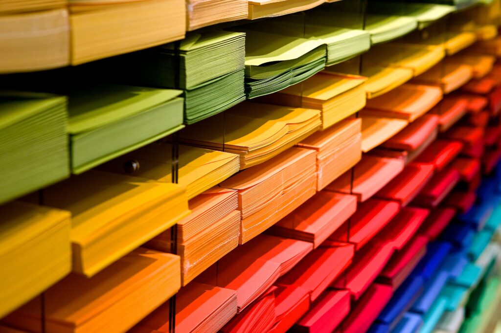 an array of different colours of paper - yellow, green, orange, red, light and dark blue - sit on exposed shelves